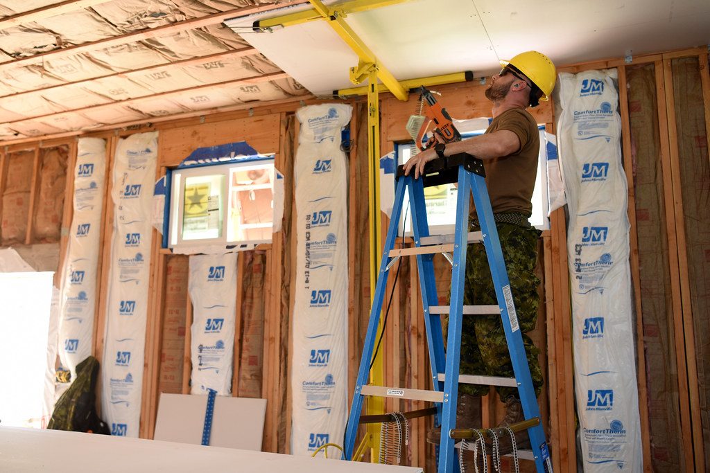 Crew hanging drywall ceiling panels with a panel lift